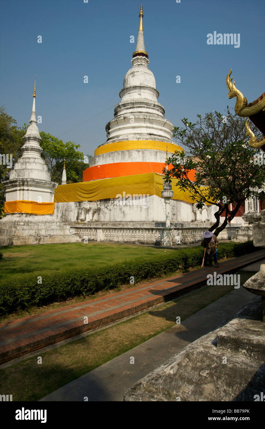 Un giardiniere passeggiate passato due chedis pietra al Wat Phra Singh in Chiang Mai Thailandia Foto Stock