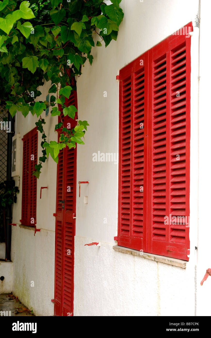 Bianco-lavato casa con persiane rosse e sportello in Port de Pollenca, Maiorca Foto Stock