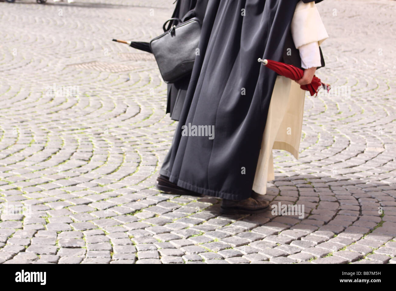 Due sacerdoti con ombrelloni passeggiate sull'acciottolato strada di Roma, Italia. Foto Stock