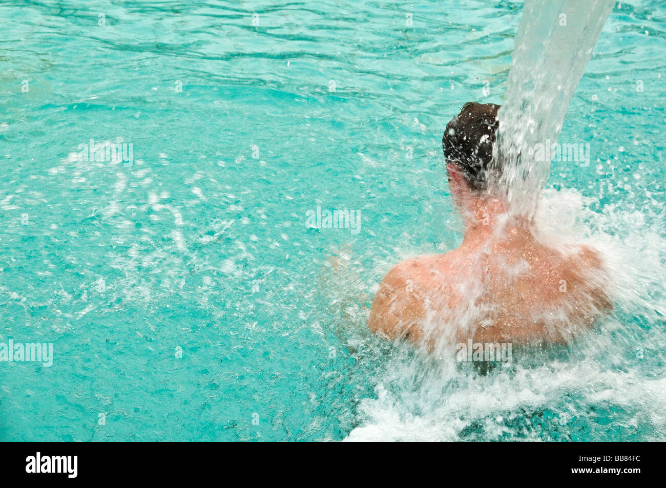 Uomo in piscina da dietro con getto massaggiante di acqua Foto Stock