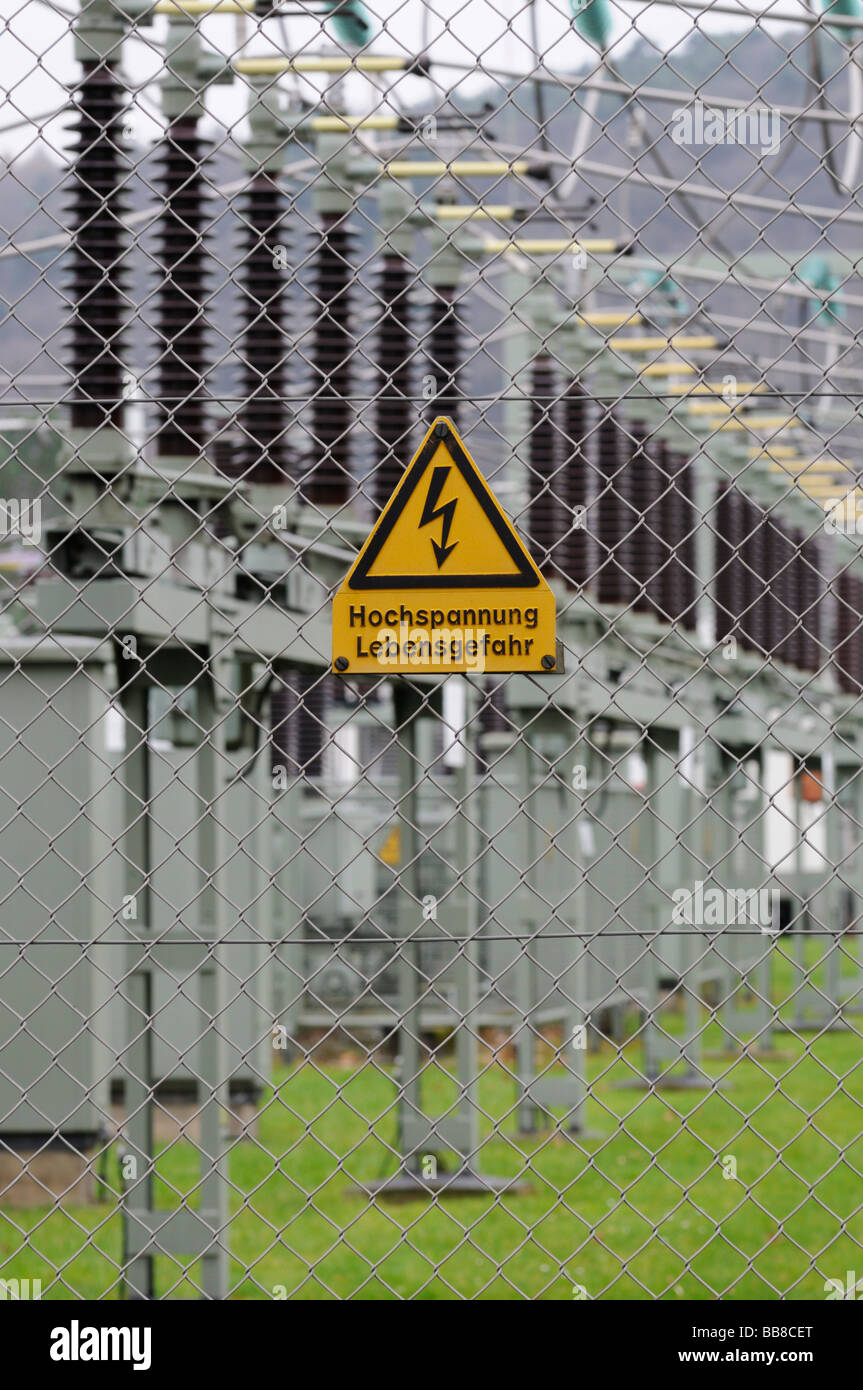 Segno, ad alta tensione e rischio di infortuni mortali, su di una maglia a filo recinzione, nella parte anteriore di un trasformatore elettrico station Foto Stock