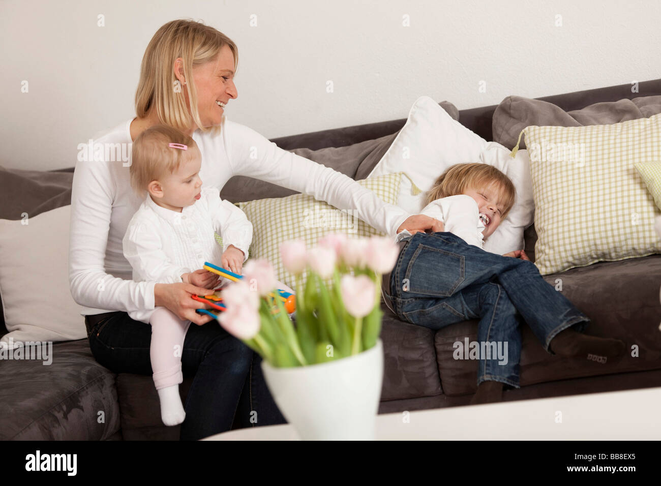 Madre con i suoi 1 anni di figlia sul suo grembo, solletico a suo figlio di 3 anni Foto Stock