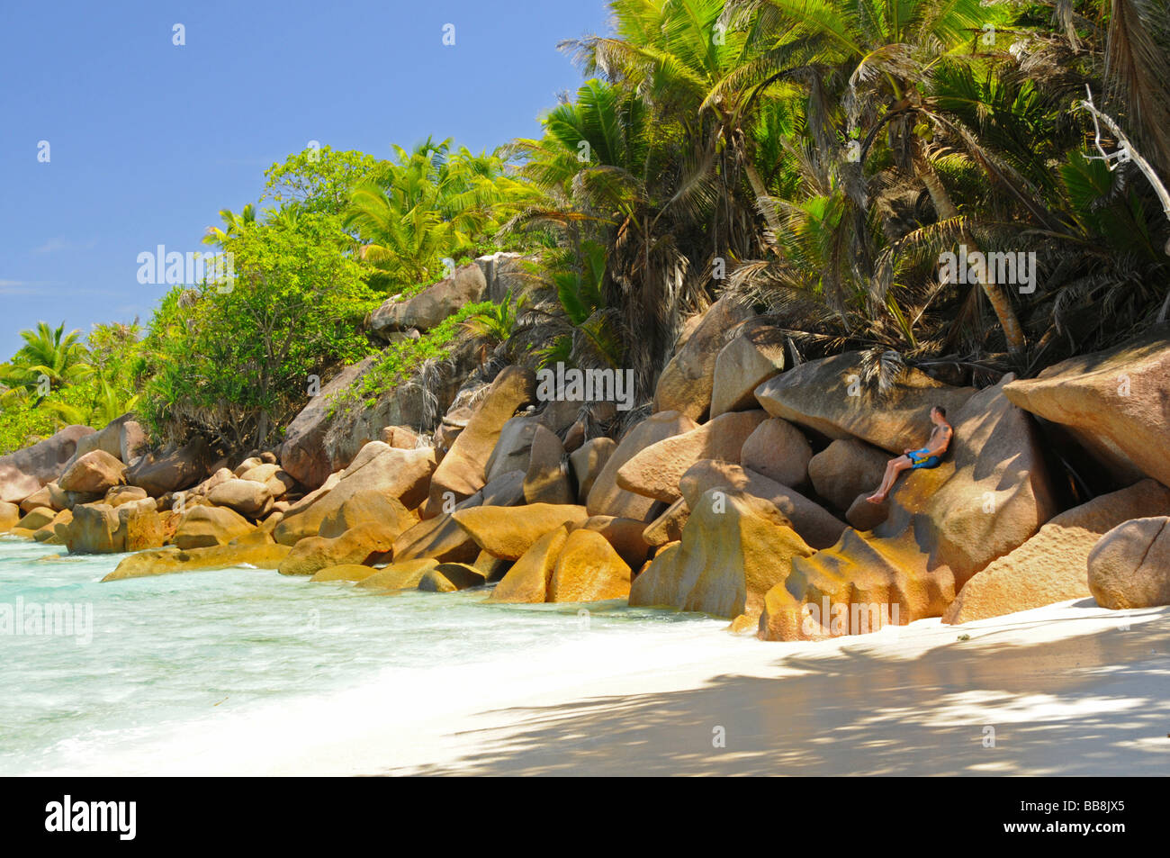 Rocce di granito e palme da cocco con un uomo a mare, Anse Cocos, La Digue, Seicelle Foto Stock