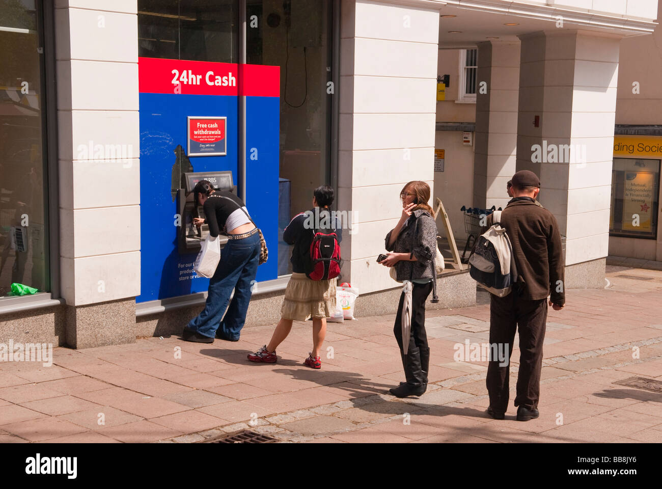 Persone queing fino a ritirare il denaro dalla Tesco bancomat foro nella parete speedbank atm in Norwich, Norfolk, Regno Unito Foto Stock