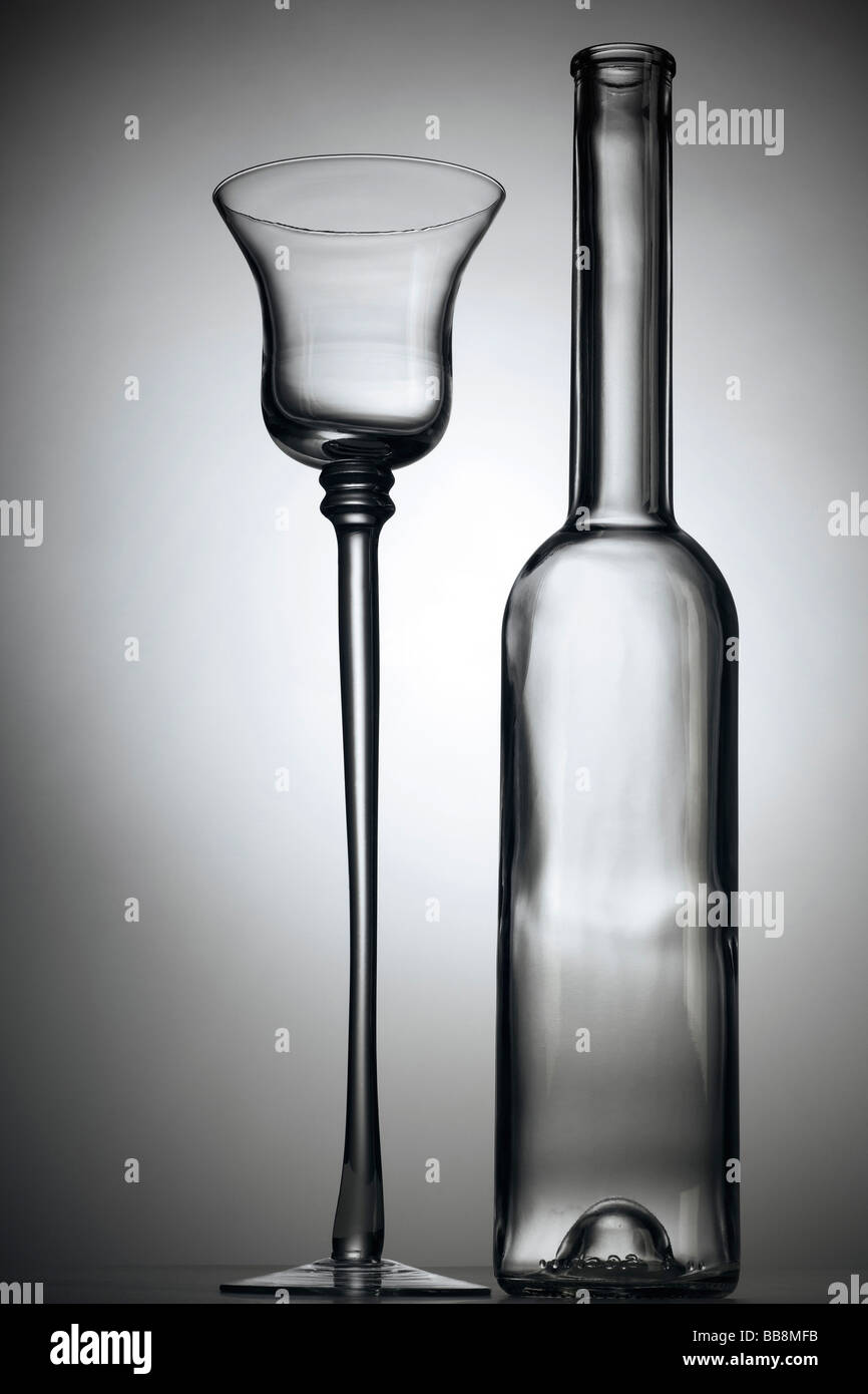 Un liquore molto alti di vetro e una bottiglia vuota contro uno sfondo grigio Foto Stock