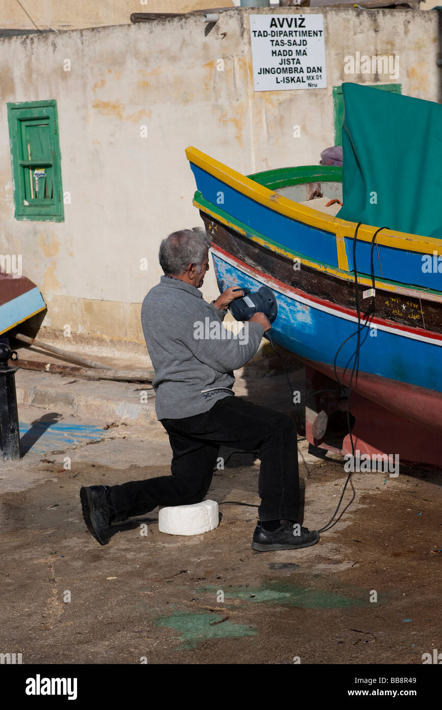 Pescatore riparando la sua barca, porto di Marsaxlokk, Malta, Europa Foto Stock