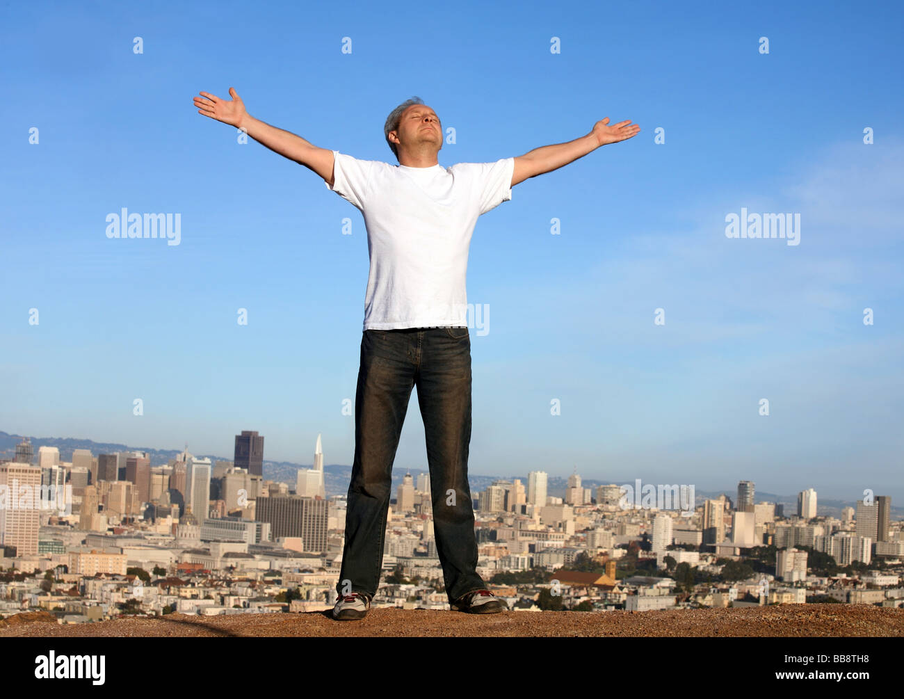 Un uomo in piedi su una collina con una vista di San Francisco con le braccia sollevate Foto Stock