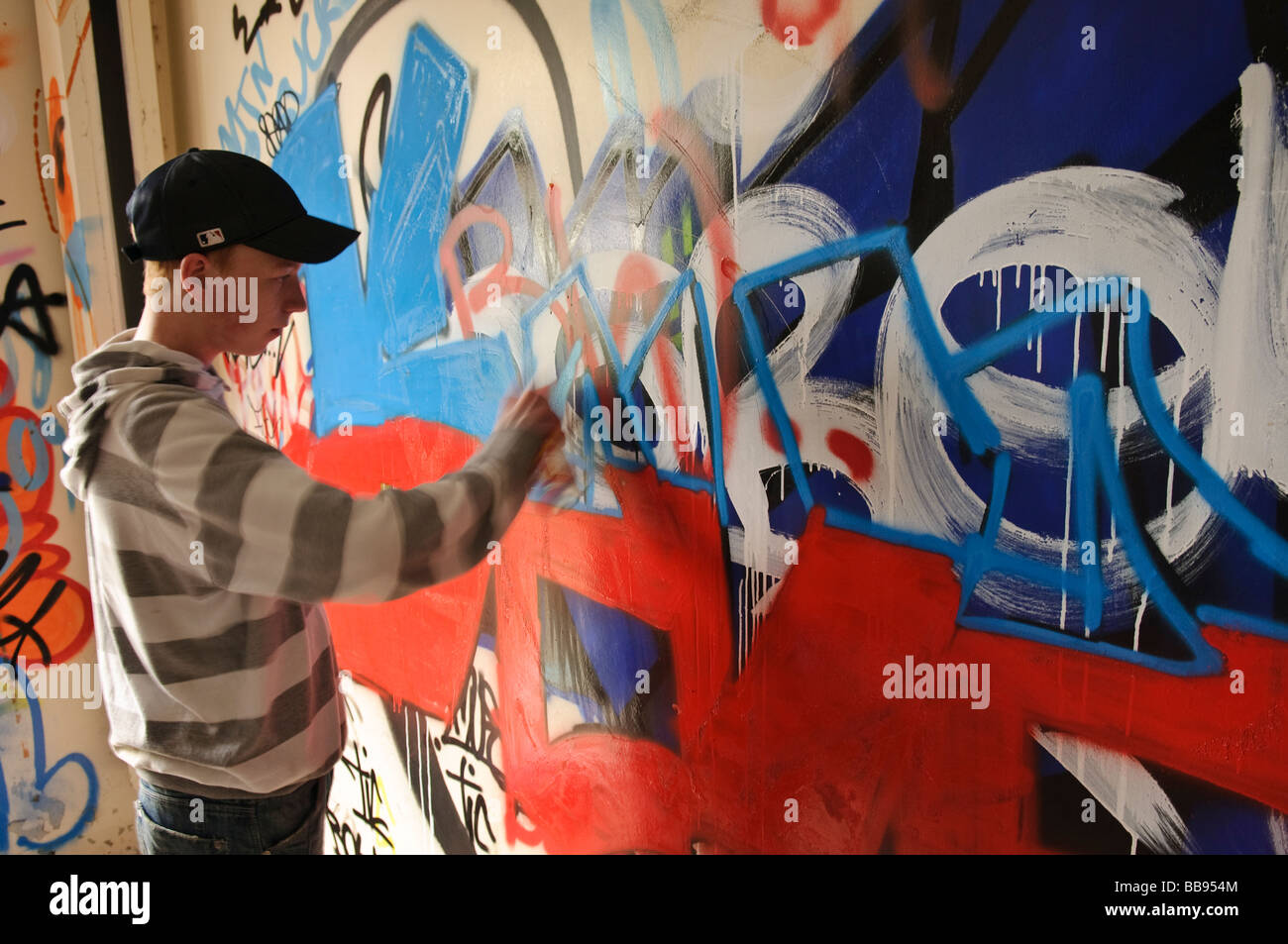 Ragazzo adolescente lavorando su un pezzo di grafitti su una parete interna. Foto Stock
