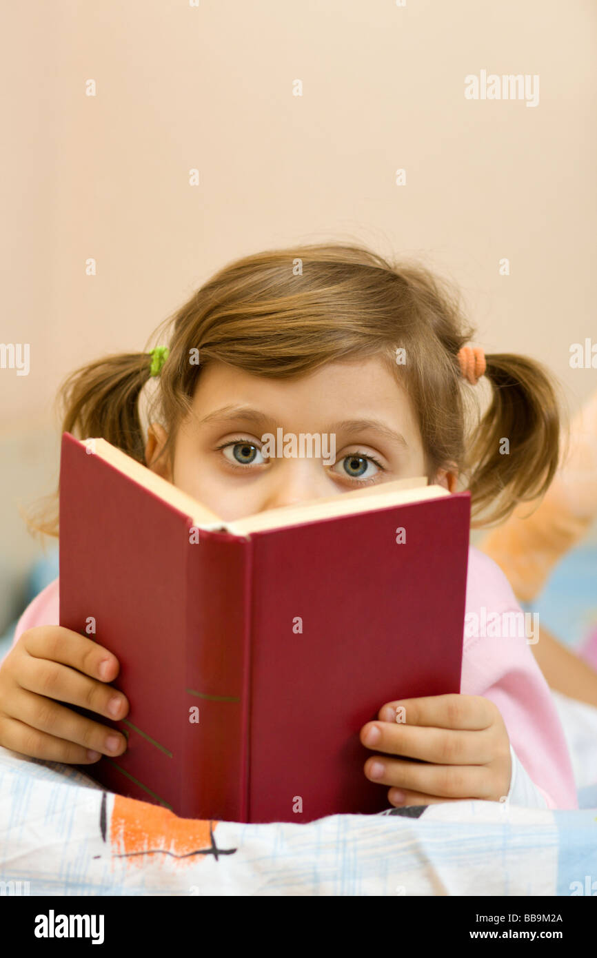 Giovane ragazza a leggere un libro sul suo letto Foto Stock