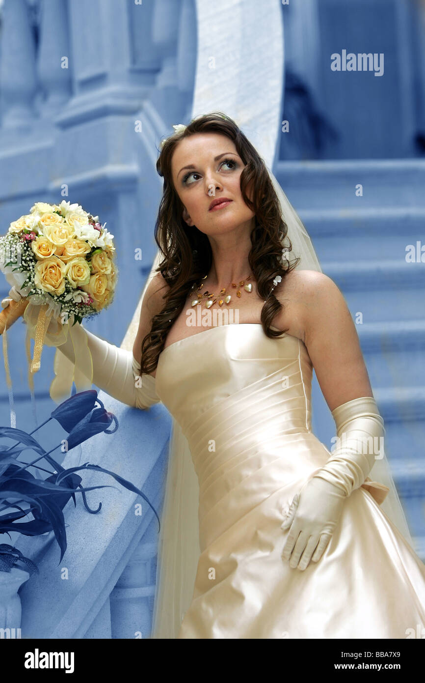 Basso angolo vista della bellissima giovane sposa con bouquet di fiori sfondo blu Foto Stock