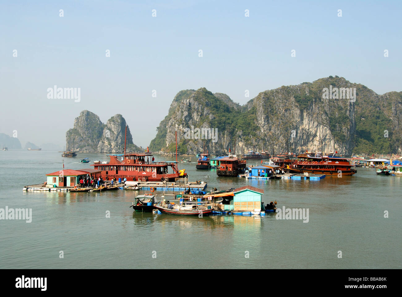 Villaggio galleggiante con case galleggianti di fronte le isole della roccia, la baia di Ha Long, Vietnam, sud-est asiatico Foto Stock