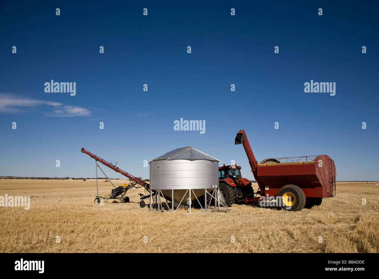 Un trattore e mietitrebbia accanto ad un contenitore di semi in un campo di grano Foto Stock