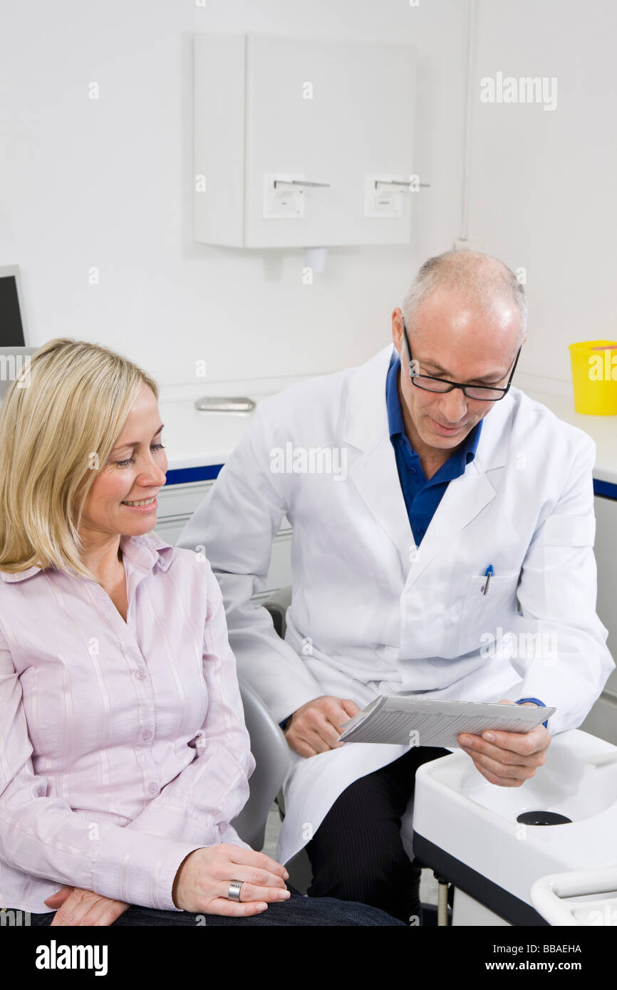 Un dentista parlando a un paziente seduto in una poltrona del dentista Foto Stock