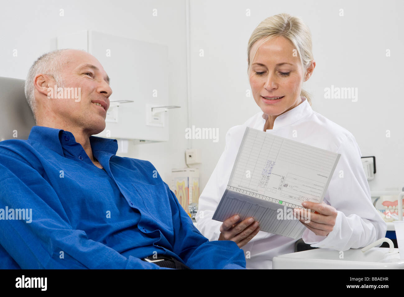 Un dentista parlando a un paziente seduto in una poltrona del dentista Foto Stock