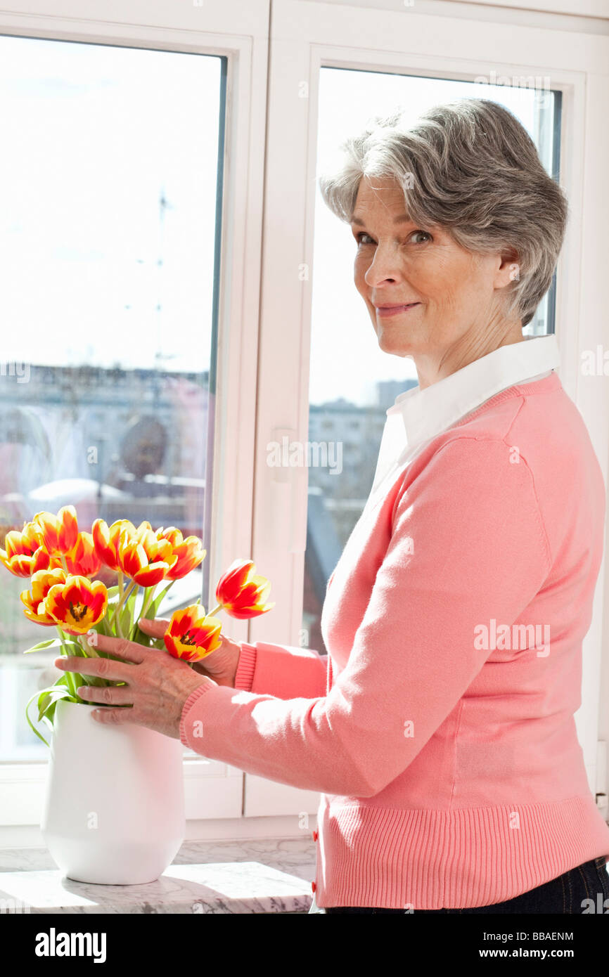 Un senior donna disponendo dei fiori in un vaso Foto Stock