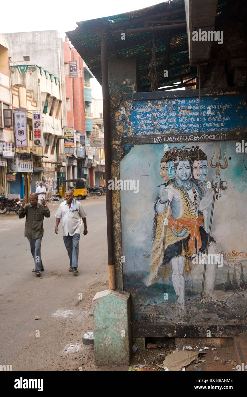 Due uomini a piedi verso un'immagine di Shiva che trasportano un tridente che è dipinta su uno schermo a Chennai, India. Foto Stock