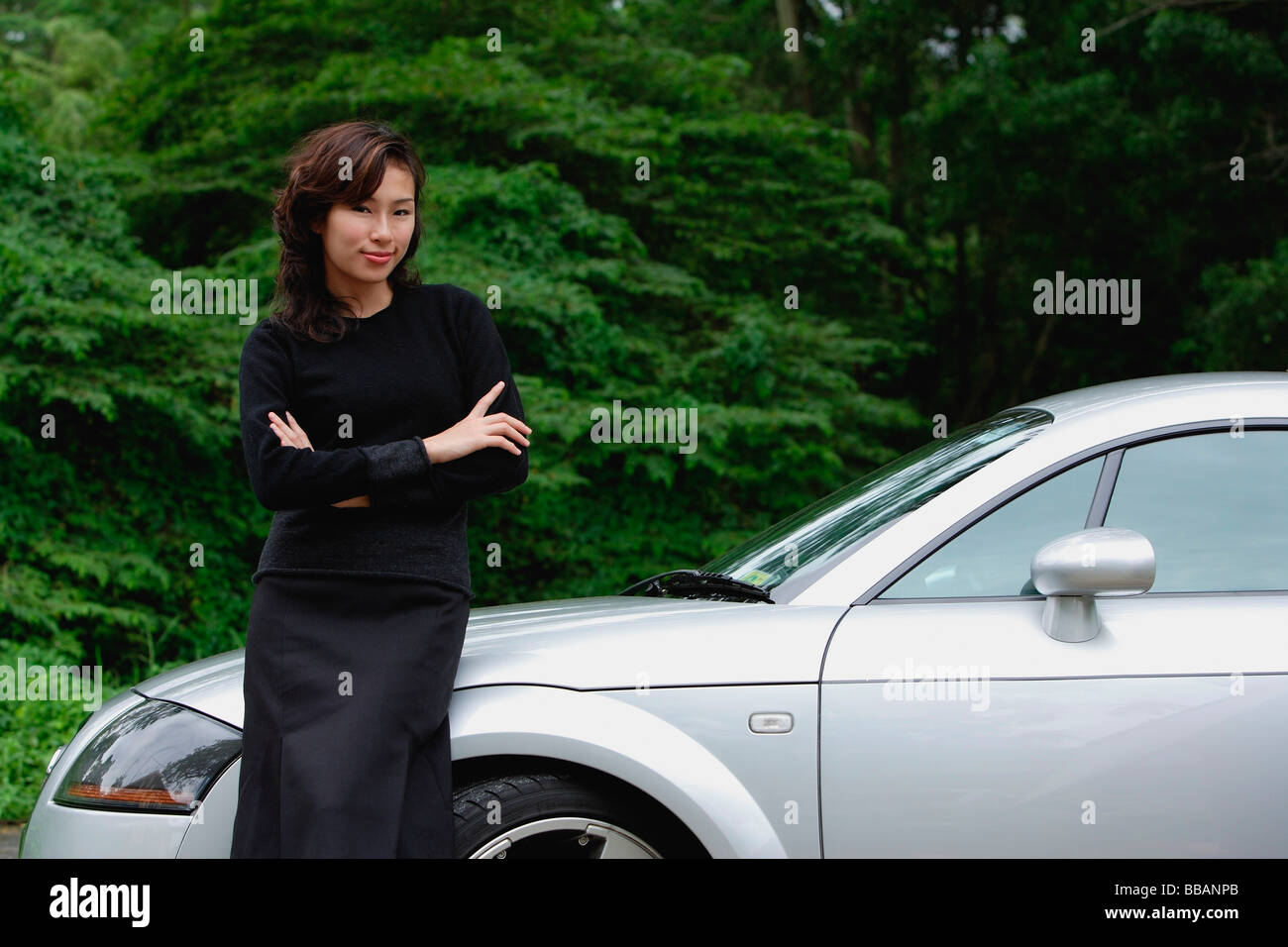 Donna appoggiata su auto sportiva, sul lato della strada, sorridente in telecamera Foto Stock