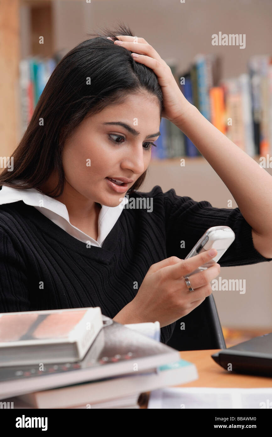 Donna in biblioteca, mano sulla testa, guardando il telefono cellulare Foto Stock