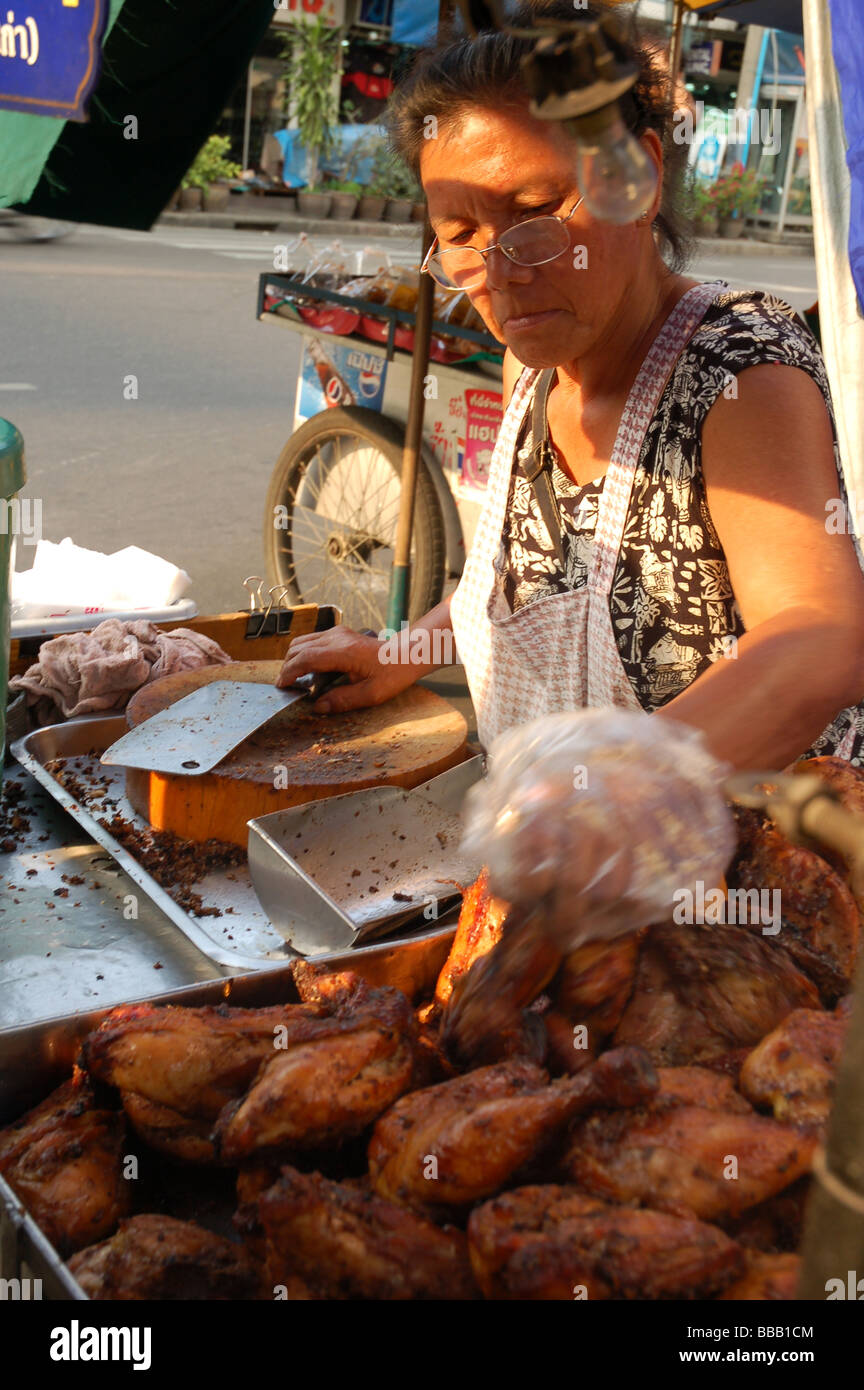 Signora tailandese alla griglia di vendita le cosce di pollo in Khao San Road, Bangkok, Thailandia Foto Stock