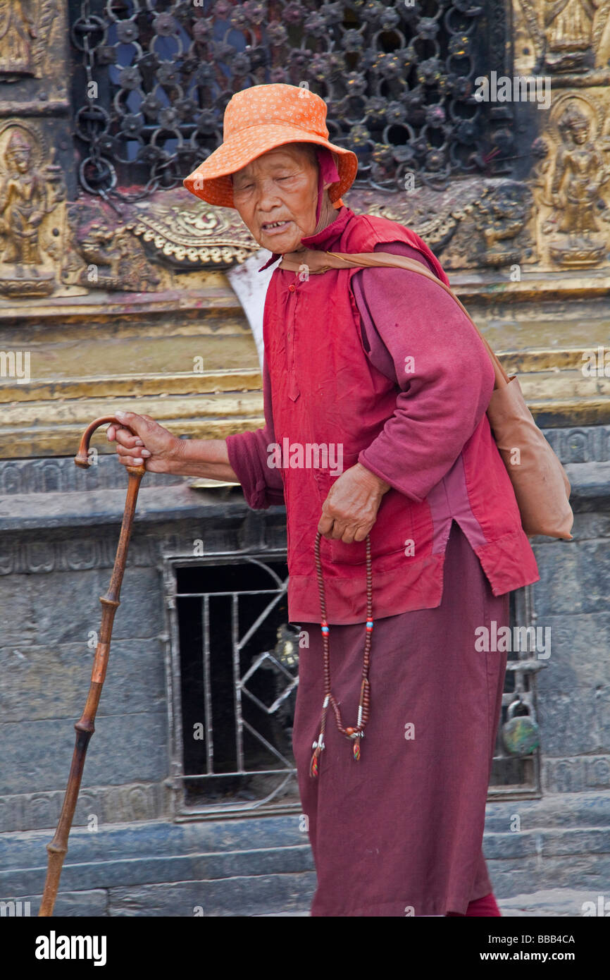 Pellegrino donna con canna vestita in rosso cappotto e mantello camminando in Nepal Kathmandu Foto Stock
