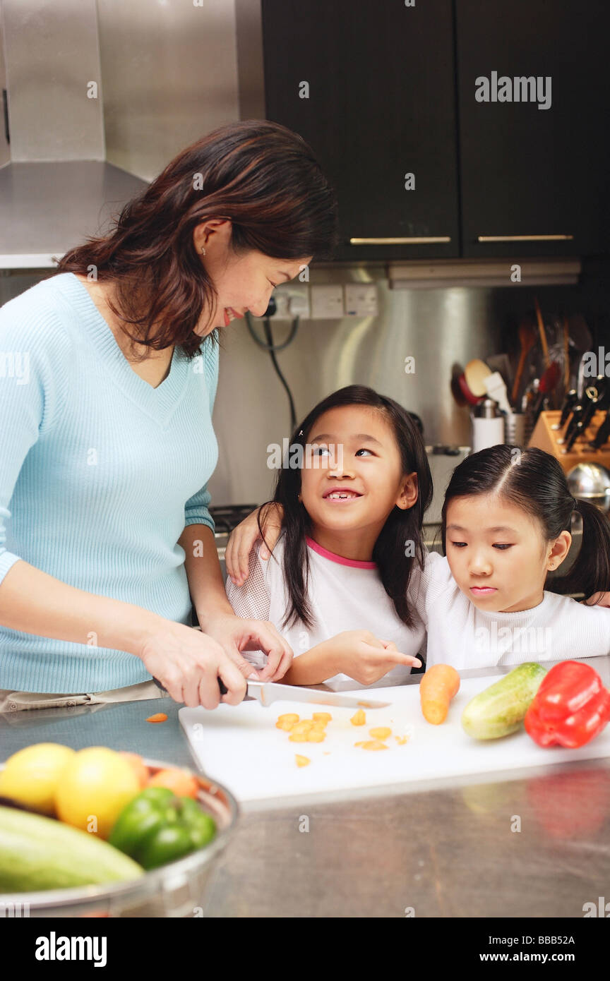 Madre come tagliare le verdure in cucina, figlie in piedi accanto a lei Foto Stock