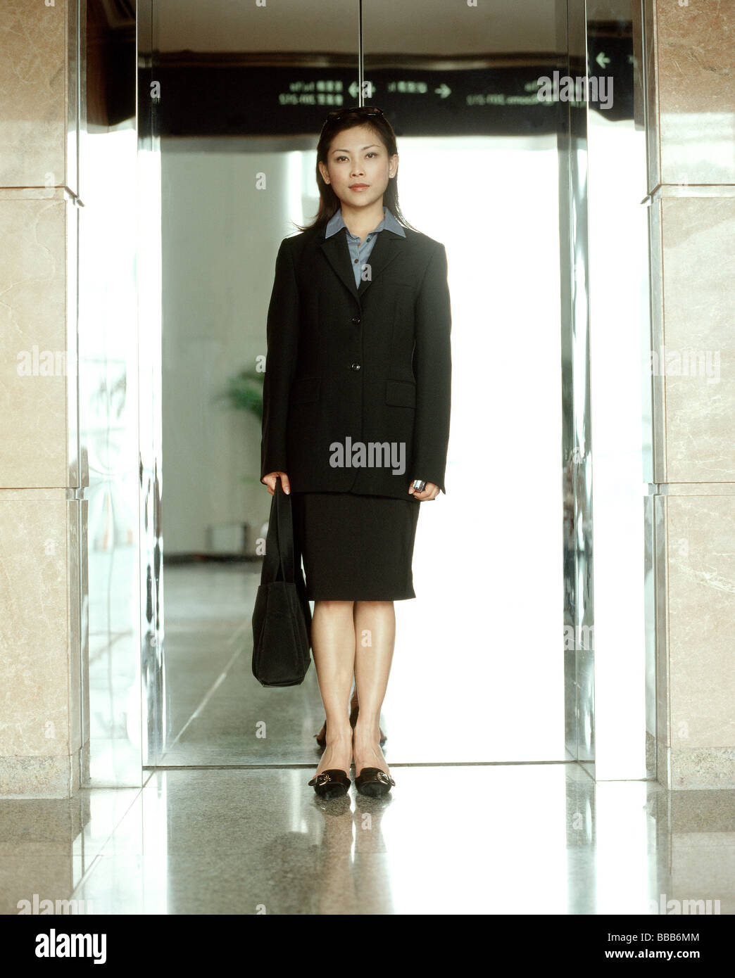 Executive donna in piedi nella parte anteriore del riflettente porte di ascensori, ritratto. Foto Stock