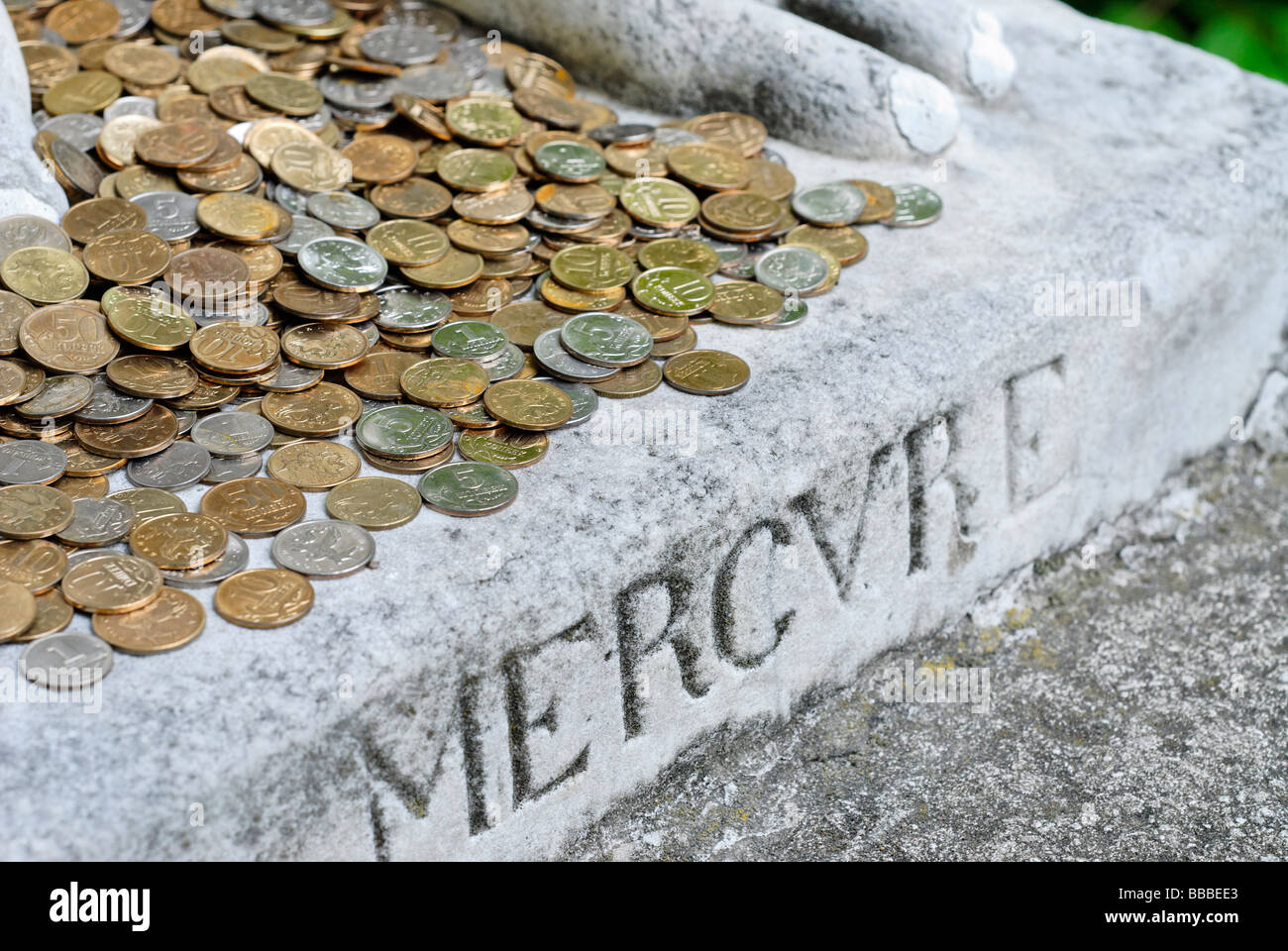 Monete metalliche in corrispondenza dei piedi di Dio statua di Mercurio Foto Stock