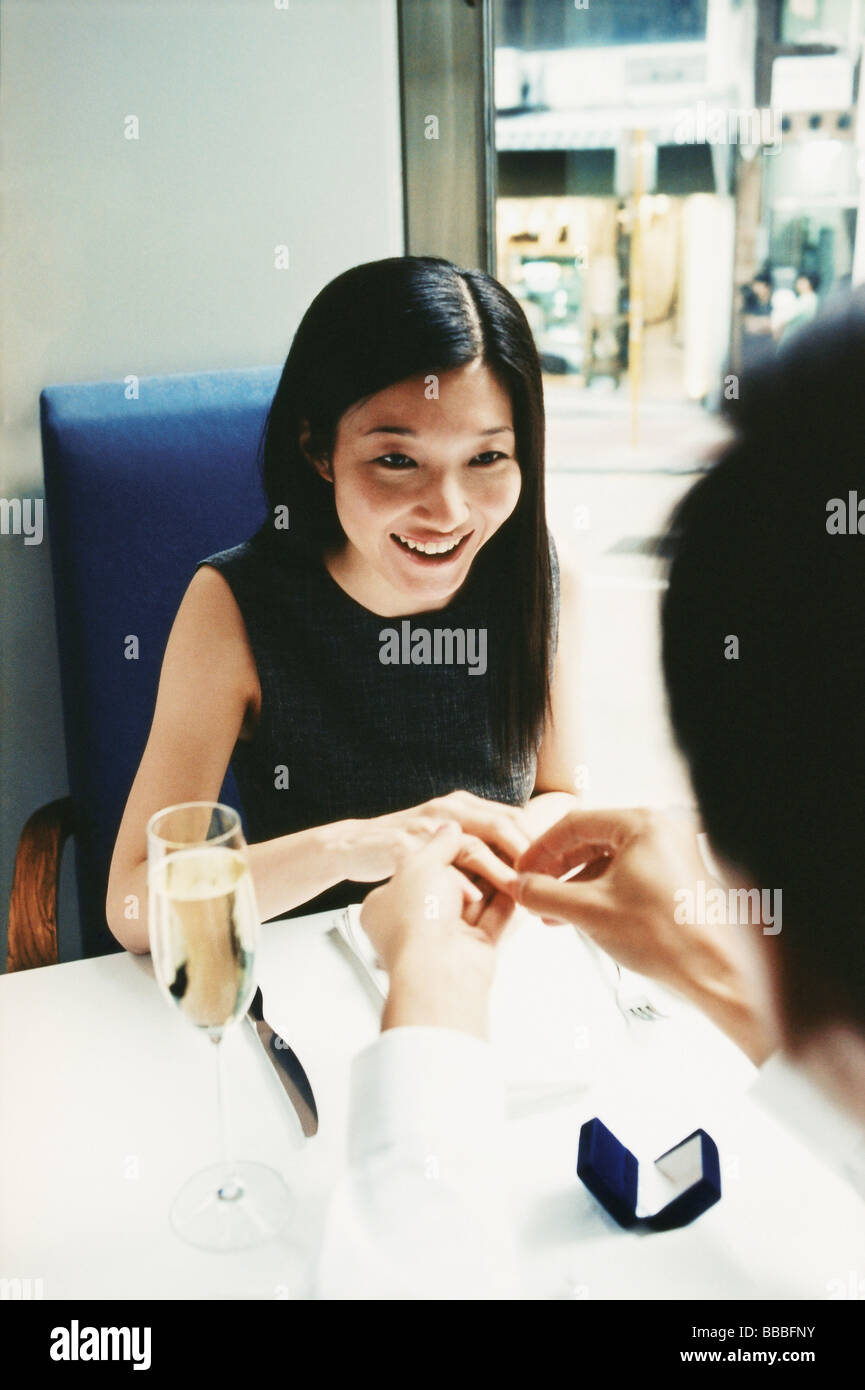 L'uomo immissione anello di fidanzamento sulla donna del dito nel ristorante Foto Stock
