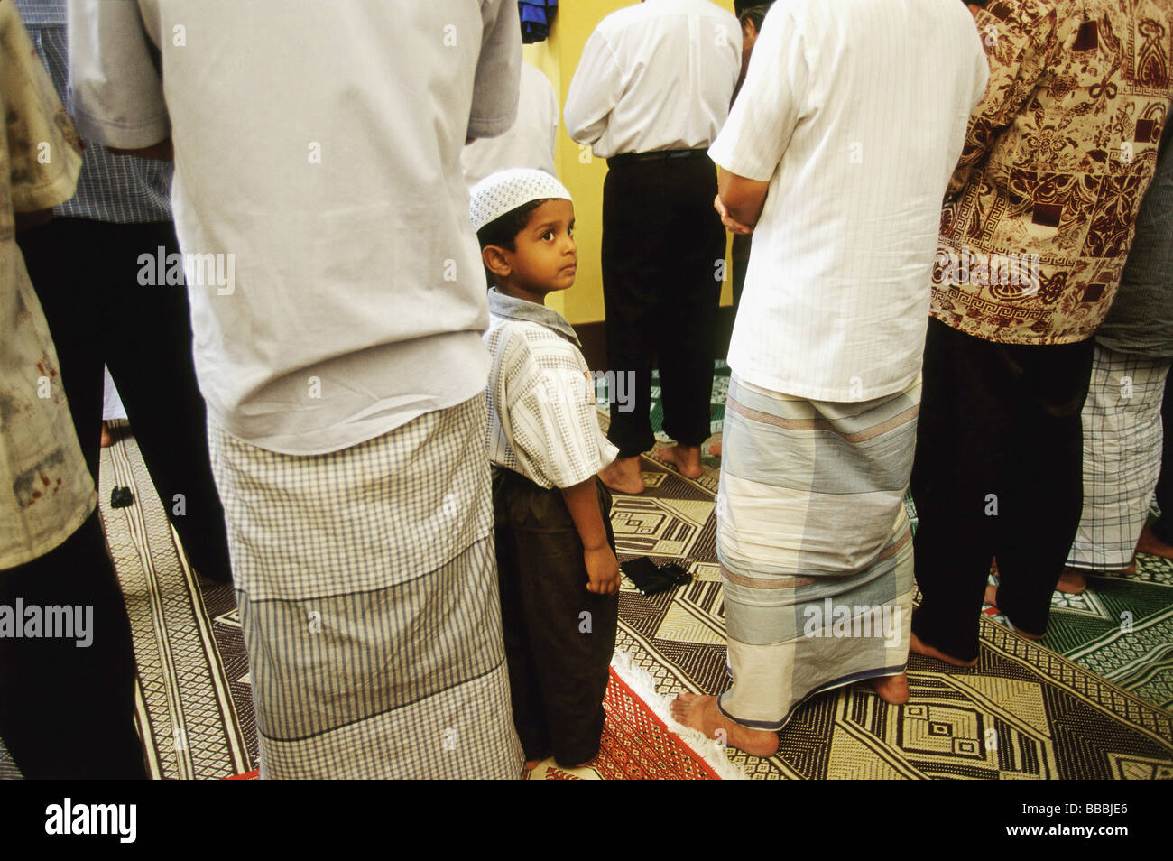 Singapore, ragazzo indossa songkok cappuccio di preghiera si erge tra gli uomini in adorazione all'Hajjah Fatimah moschea. Foto Stock