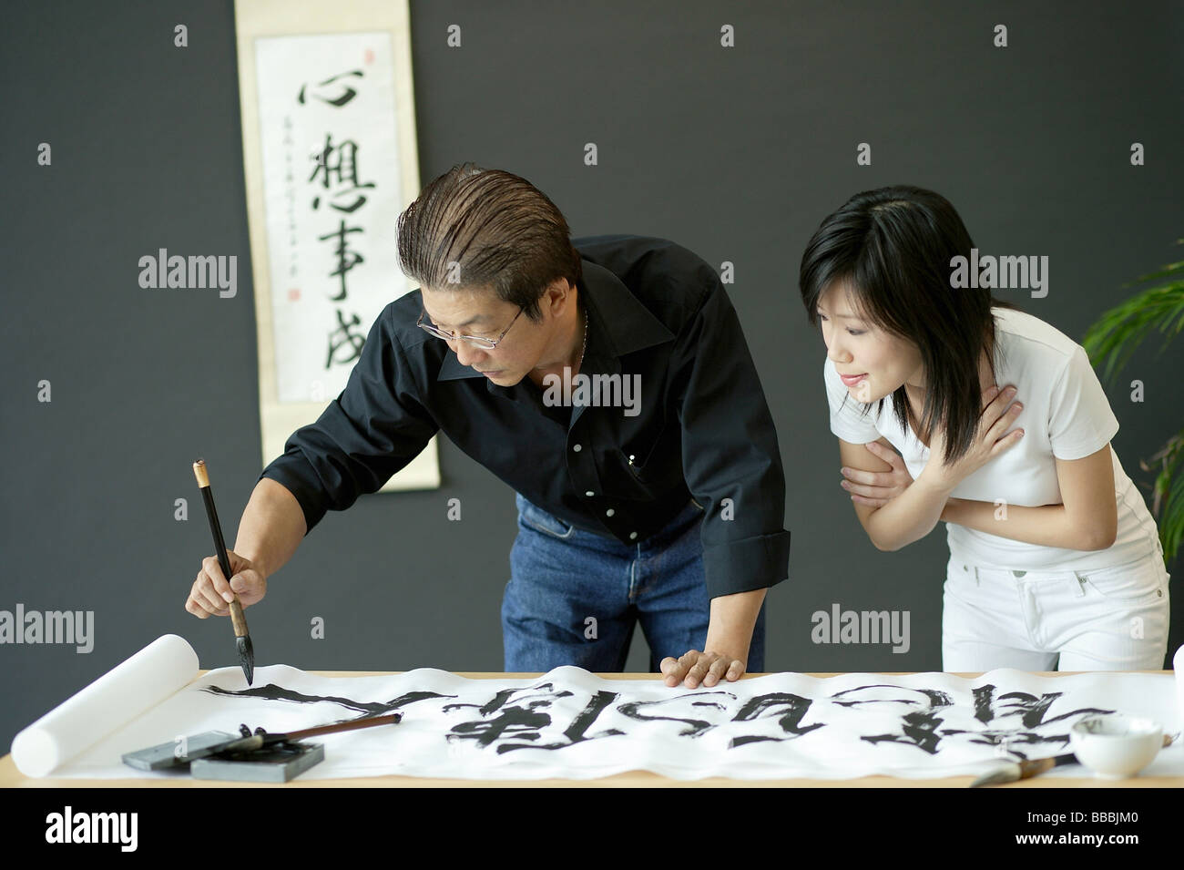 Uomo maturo pittura calligrafia cinese, la donna accanto a lui a guardare Foto Stock