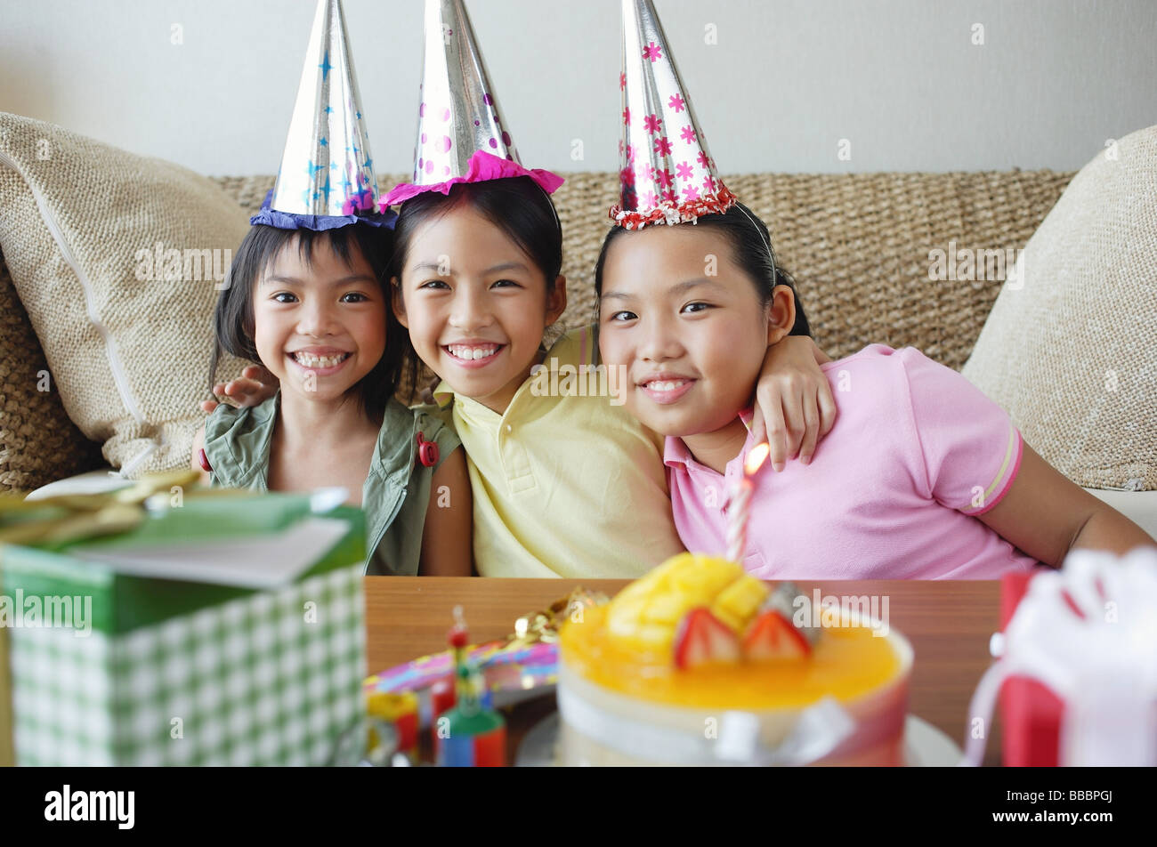 Tre ragazze con cappelli di partito seduti fianco a fianco Foto Stock