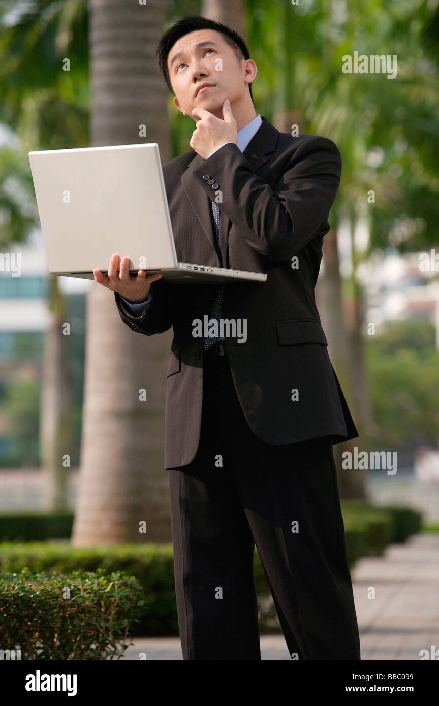 Imprenditore con espressione quizzical, tenendo il laptop e guardando in alto Foto Stock