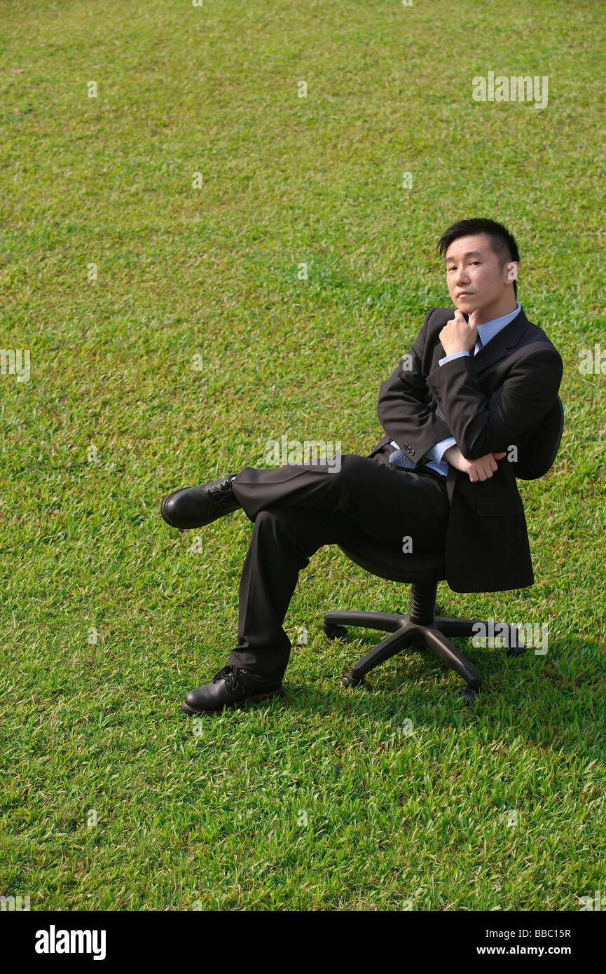Imprenditore con espressione quizzical seduto sulla sedia da ufficio Foto Stock