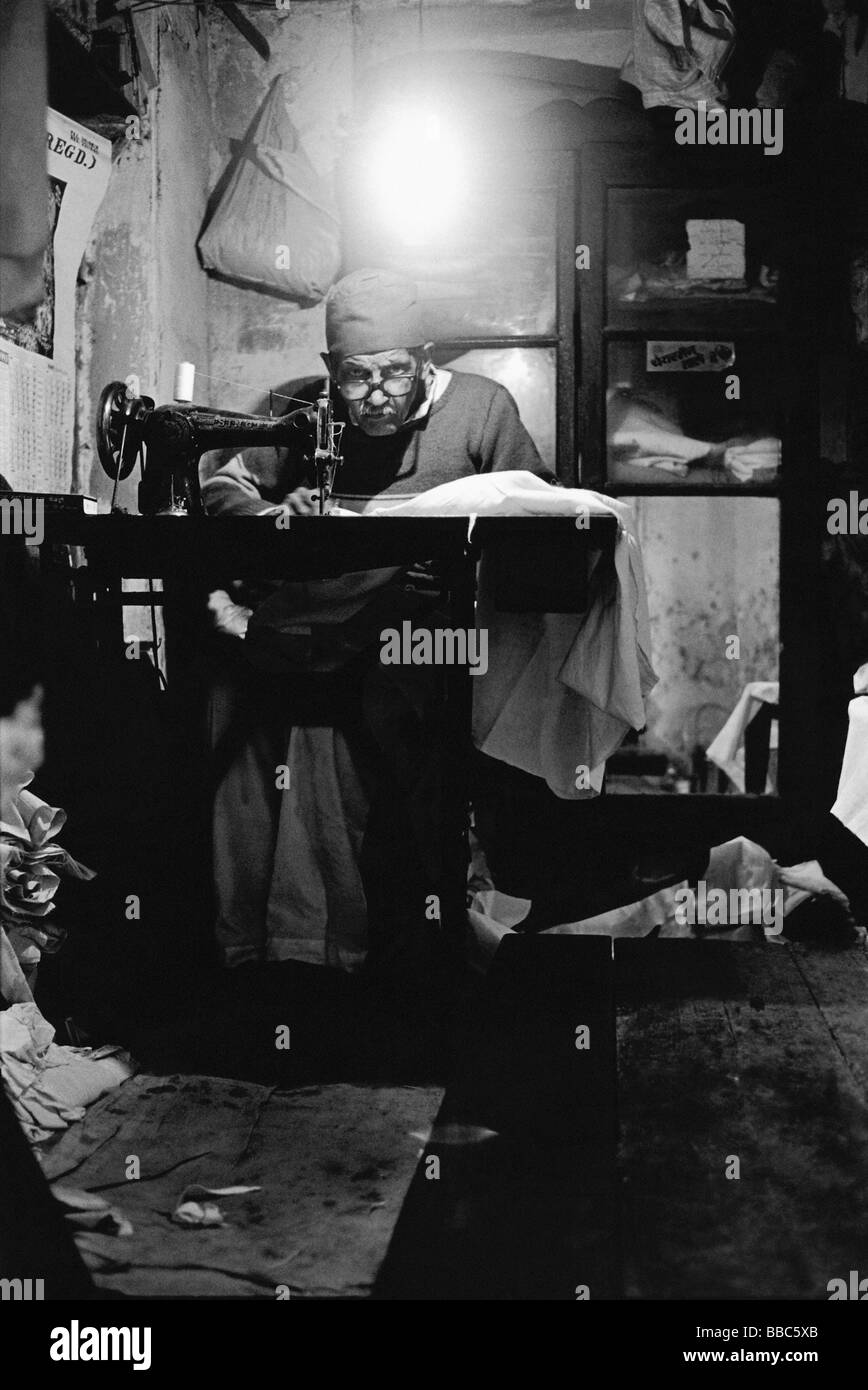 India, Vecchia Delhi, uomo anziano alla macchina da cucire in piccolo negozio. Foto Stock