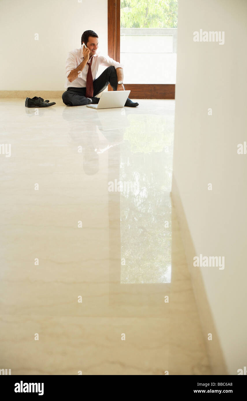 Imprenditore sul pavimento con un telefono cellulare e lap top Foto Stock
