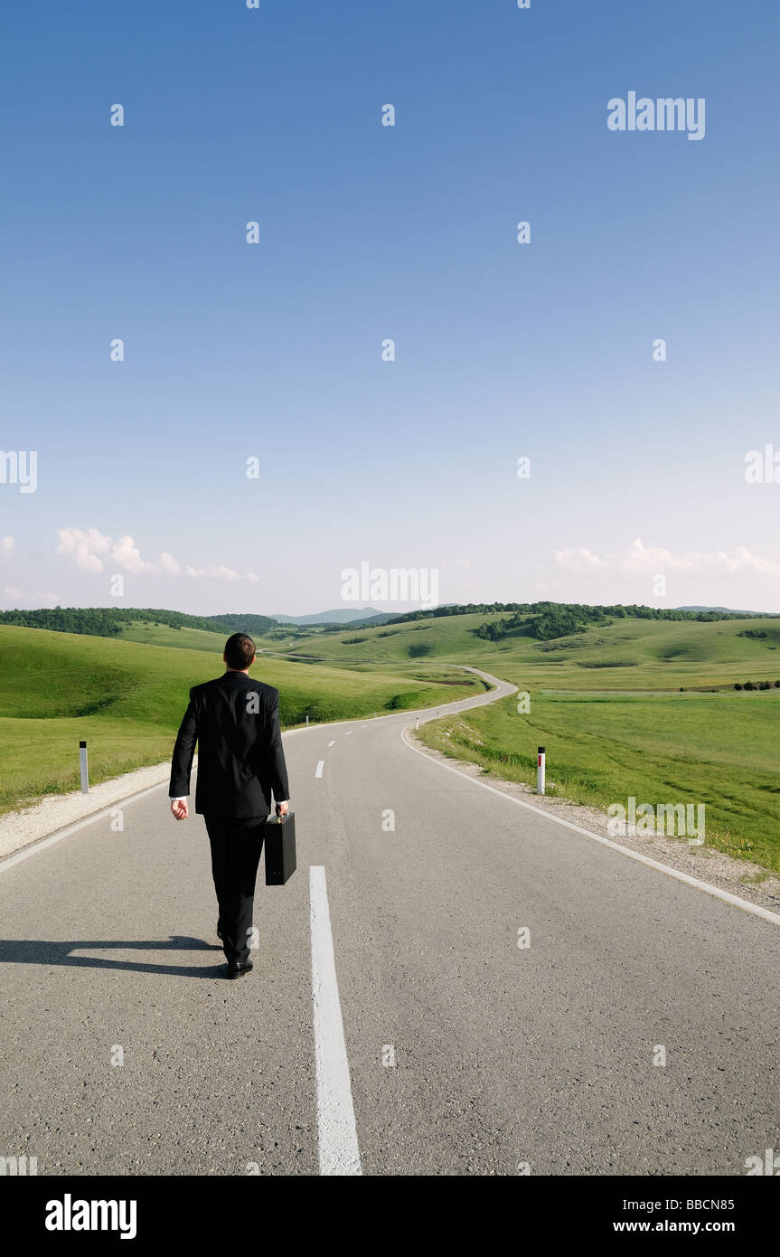 Imprenditore a piedi lungo un paese isolato su strada vista posteriore Foto Stock
