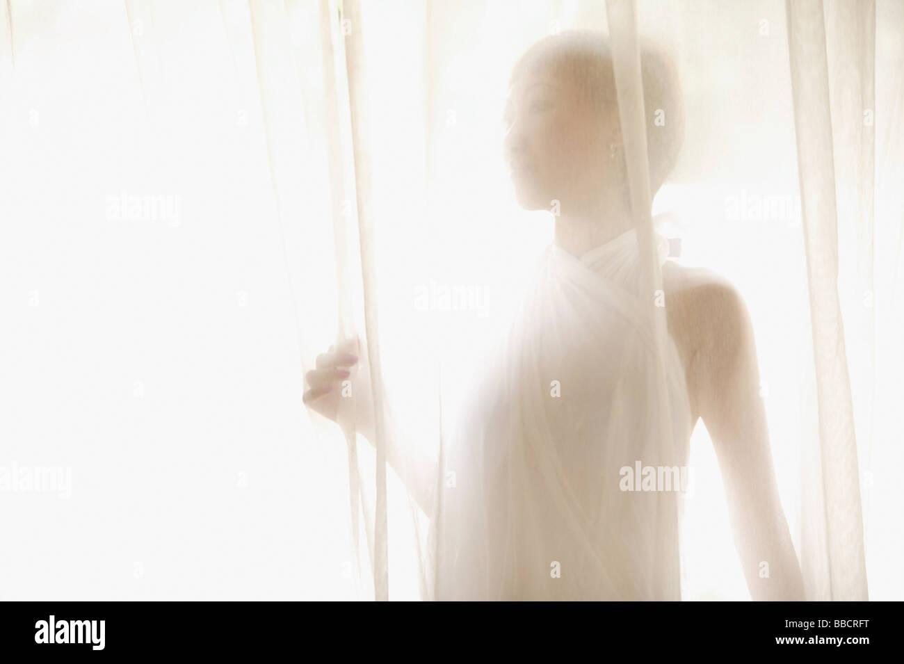 Giovane donna in piedi dietro la cortina Foto Stock