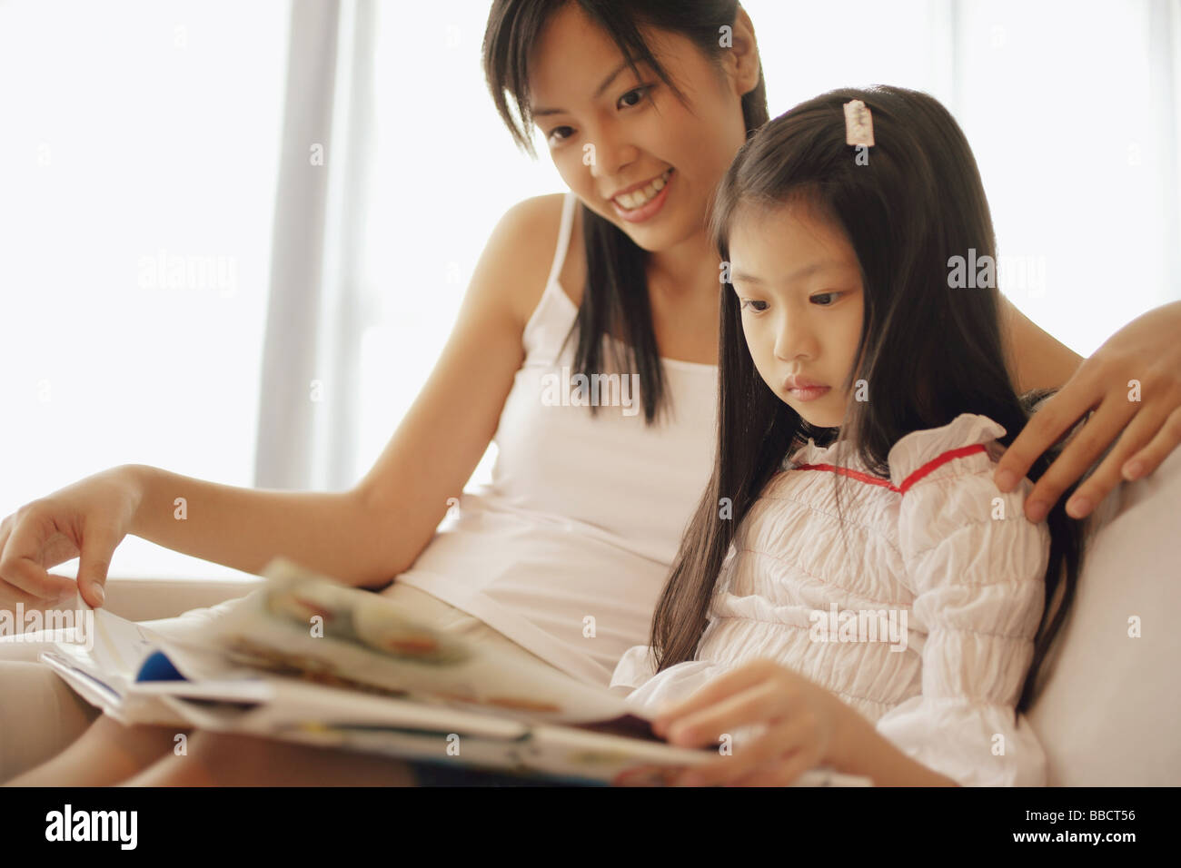 Madre e figlia seduti fianco a fianco, guardando il libro Foto Stock