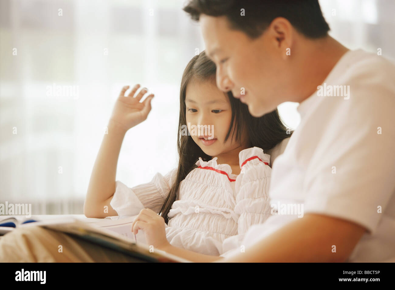 Padre e figlia seduti fianco a fianco, guardando il libro Foto Stock