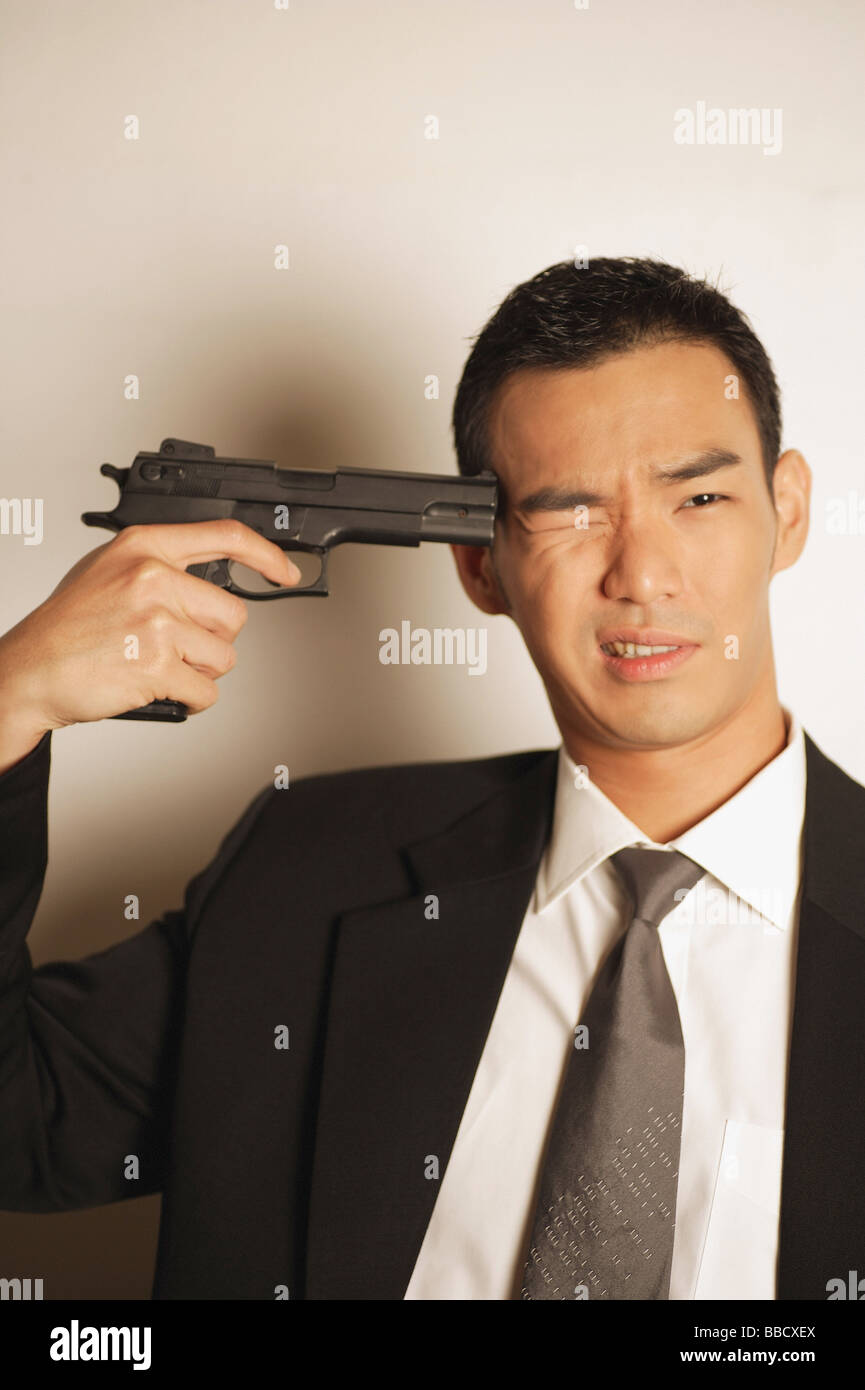 Uomo vestito con una tuta, puntando la pistola alla testa, un occhio chiuso Foto Stock