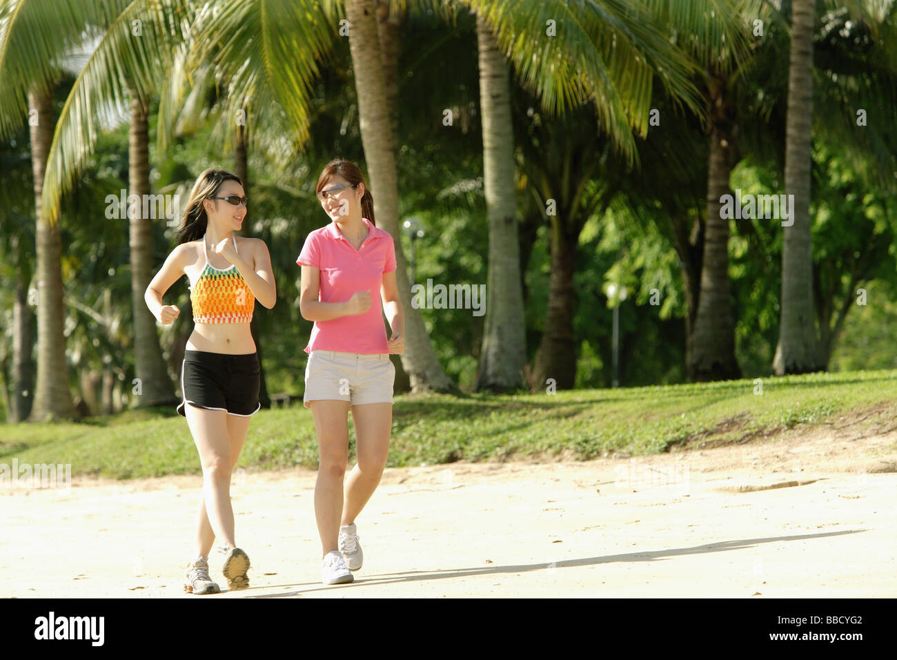 Due donne jogging lungo la spiaggia, fianco a fianco Foto Stock