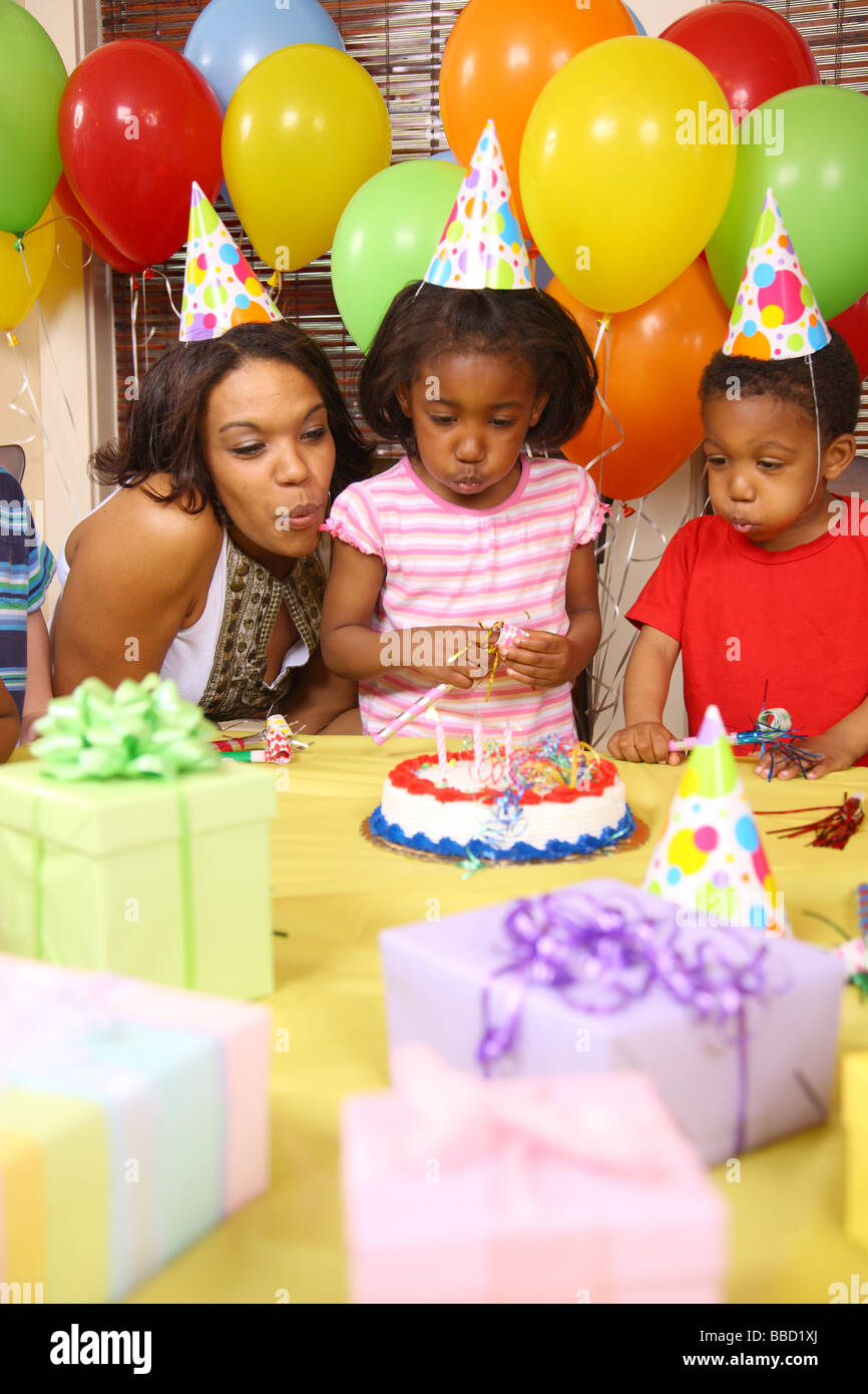 Giovane ragazza che spegne le candeline sulla torta del compleanno con aiuto dalla madre e fratello Foto Stock