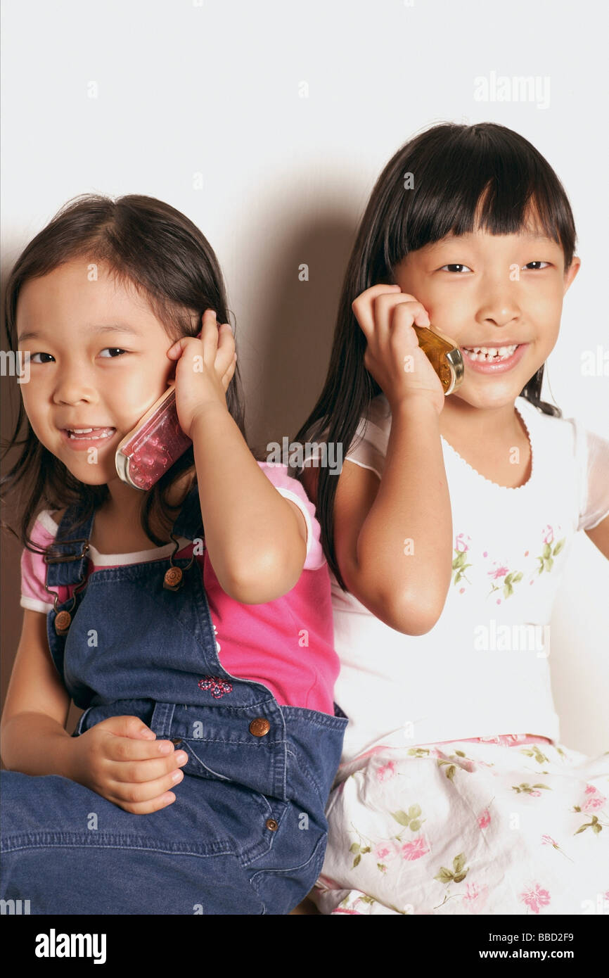 Le giovani ragazze seduti fianco a fianco i telefoni di contenimento Foto Stock