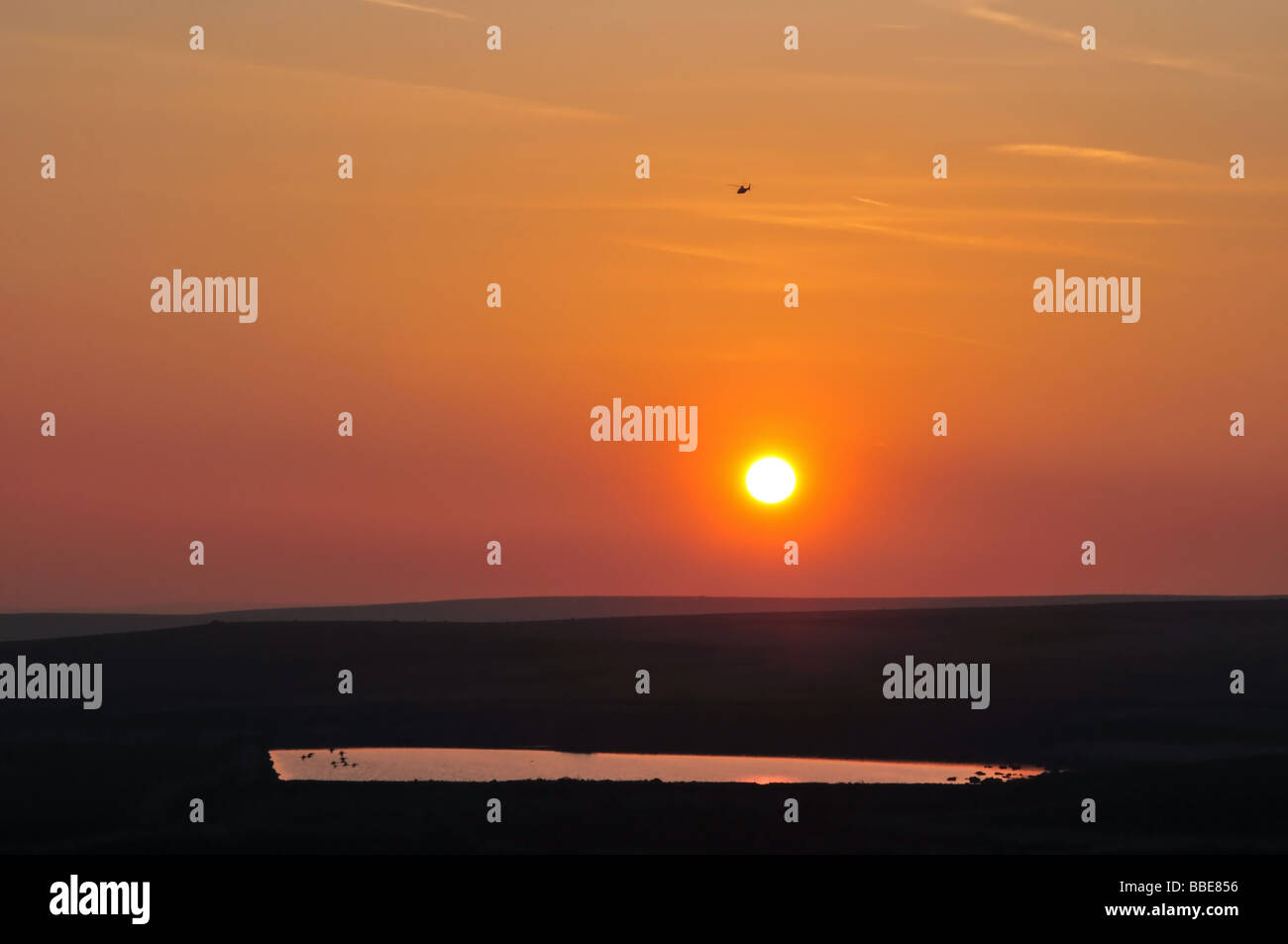 Un elicottero vola alto su un piccolo lago verso un tramonto Pennine, a ovest di Halifax, Regno Unito Foto Stock