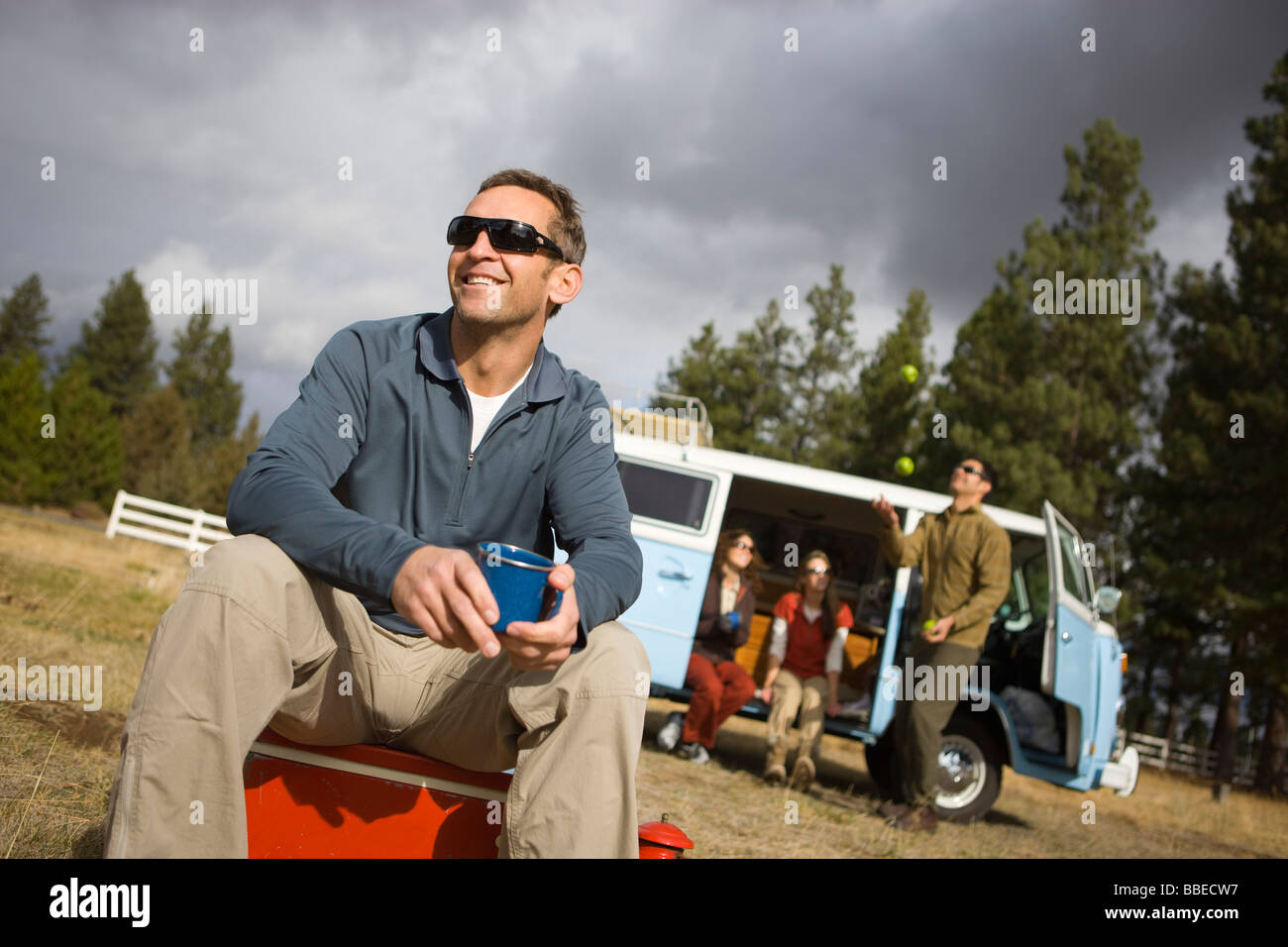 Gruppo di amici per un viaggio di campeggio, uomo seduto su un raffreddatore di bere caffè, piegare, Oregon, Stati Uniti d'America Foto Stock