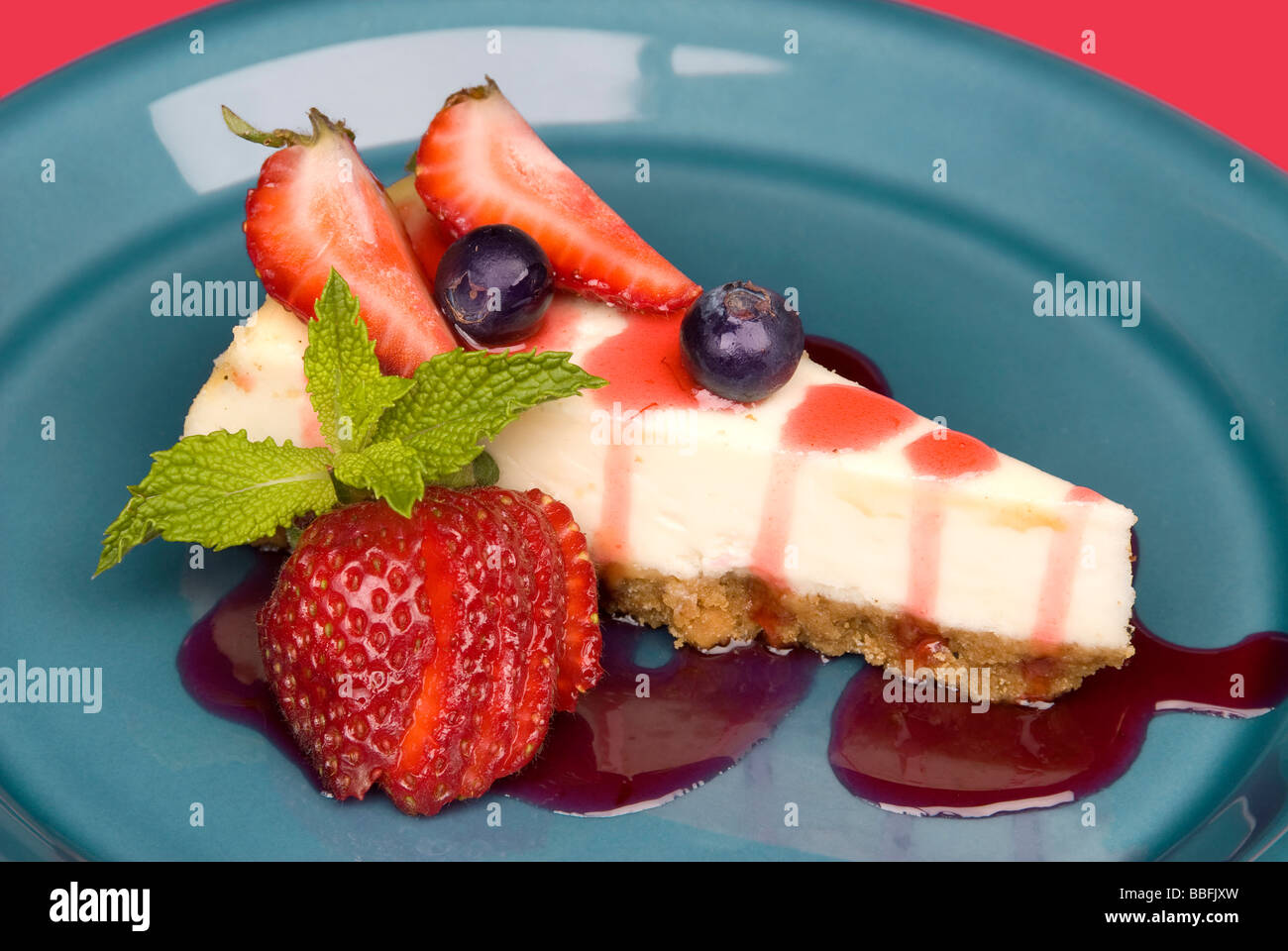 Un dessert fetta di Strawberry Cheesecake con frutta guarnite di foglie di menta e fragola salsa topping Foto Stock