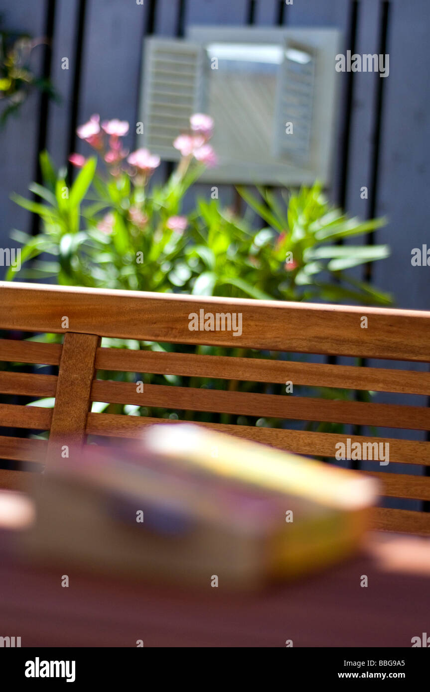 Una panchina da giardino in estate al sole con un libro su un tavolo in primo piano Foto Stock