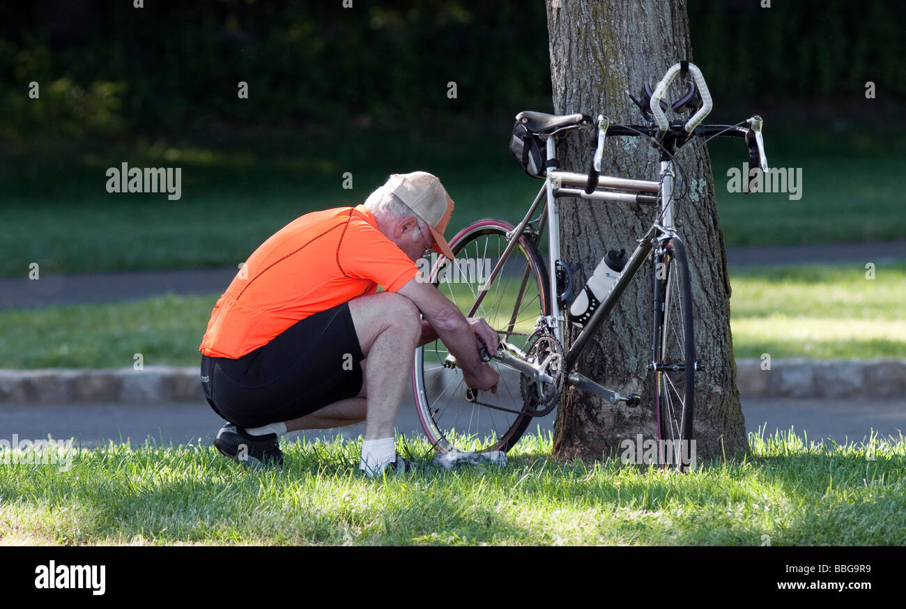 Un uomo anziano con un cappuccio di regolare la catena sulla sua bicicletta da turismo. Foto Stock