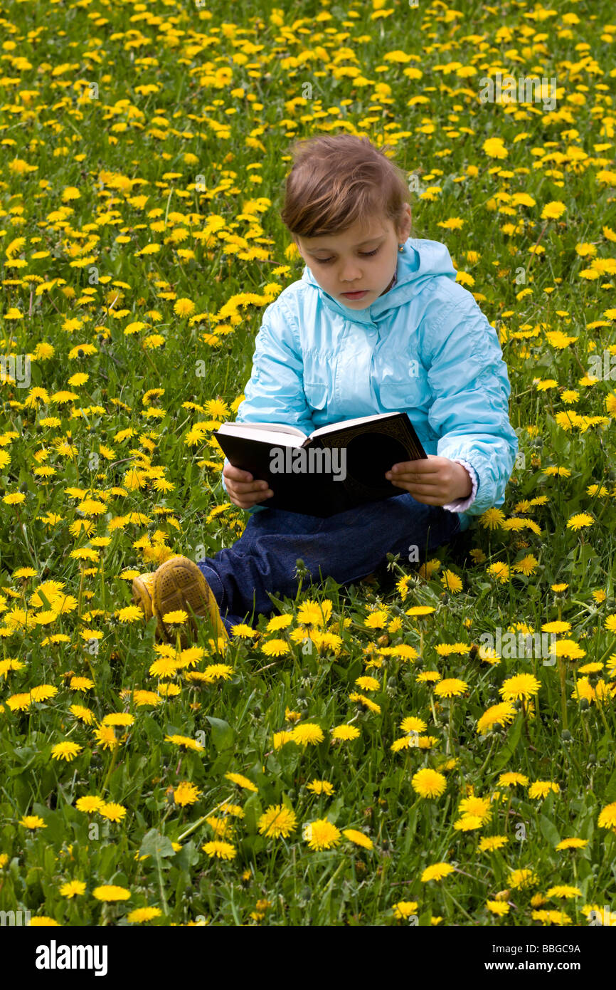 Piccola ragazza caucasica sull'erba con fiori gialli libro di lettura Foto Stock