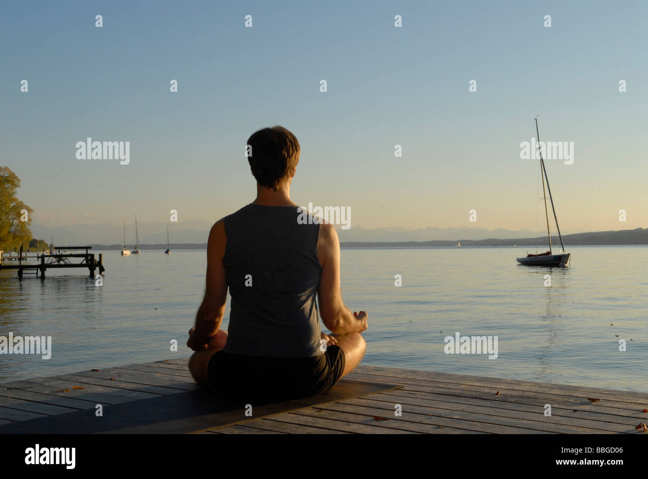 L'uomo fare yoga su un molo in legno da un lago Foto Stock